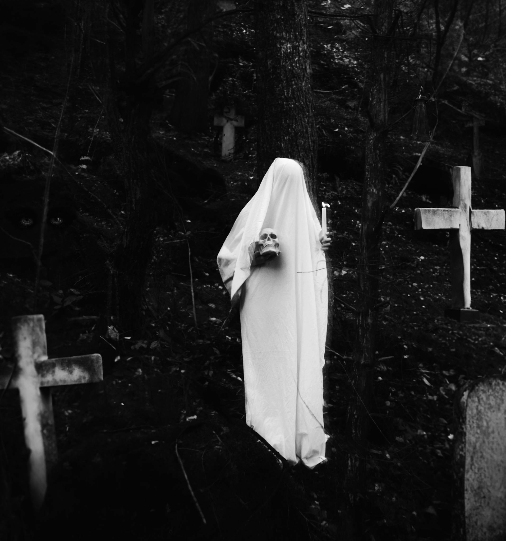 A haunting ghostly figure holding a skull and candle in a dark cemetery.