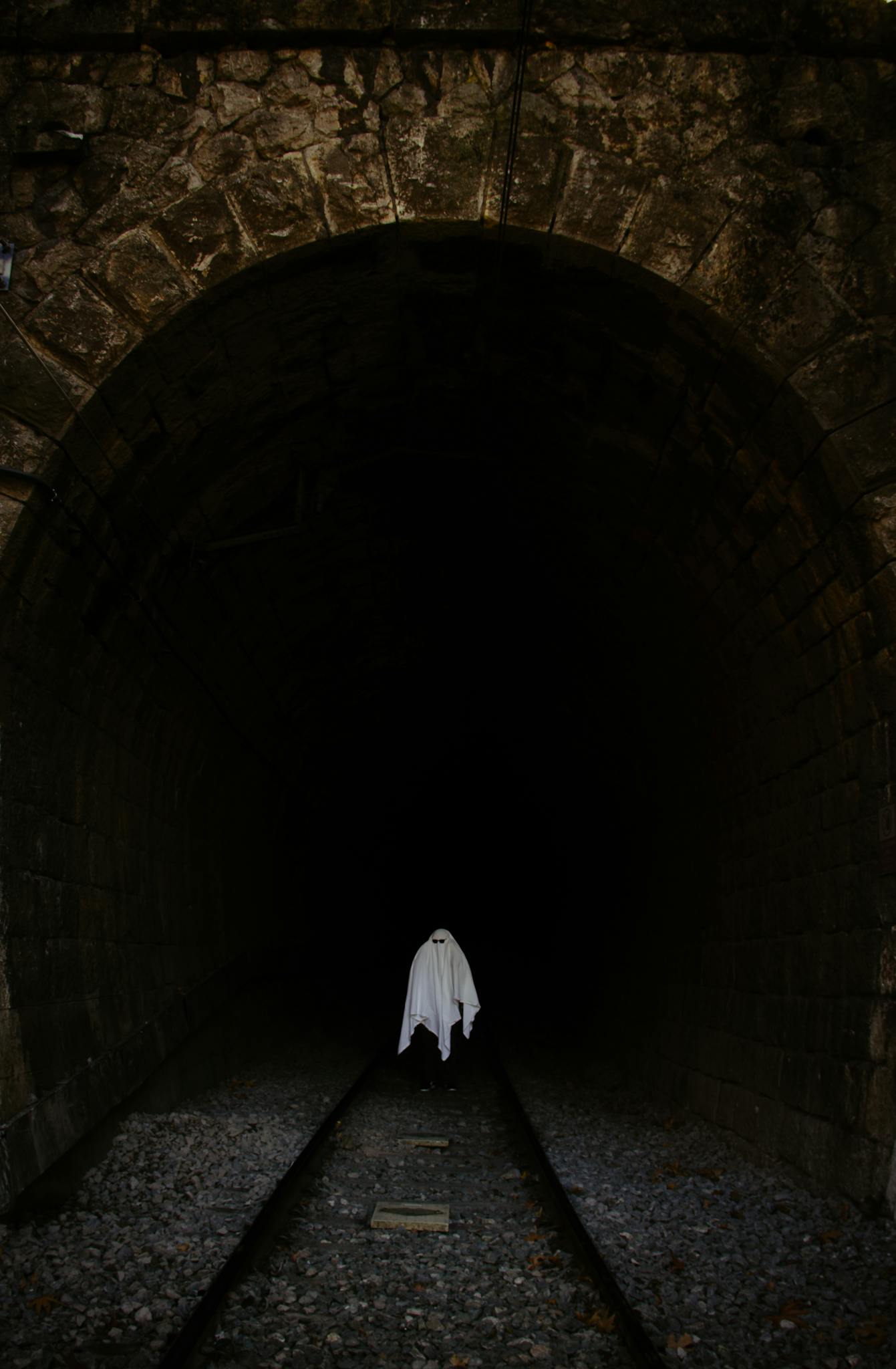 Eerie ghost costume in a dark train tunnel setting, perfect for Halloween themes.