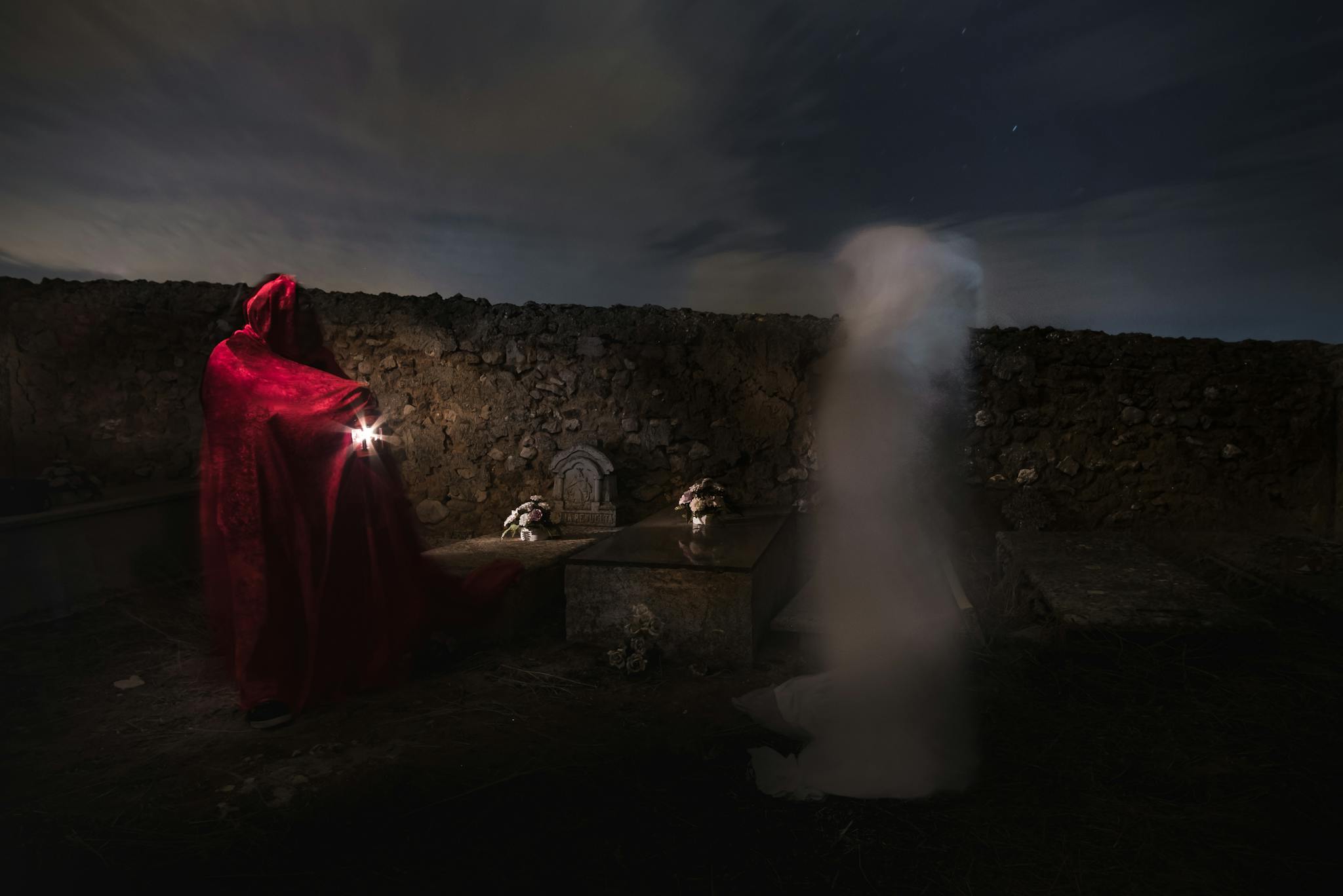 Mysterious night scene in a graveyard with a spectral figure and person in red cloak.