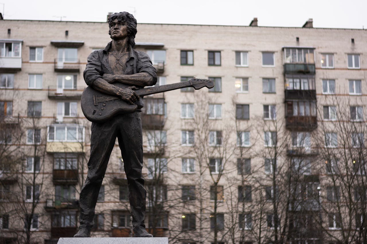 Statue of a musician with guitar in urban setting with residential building.